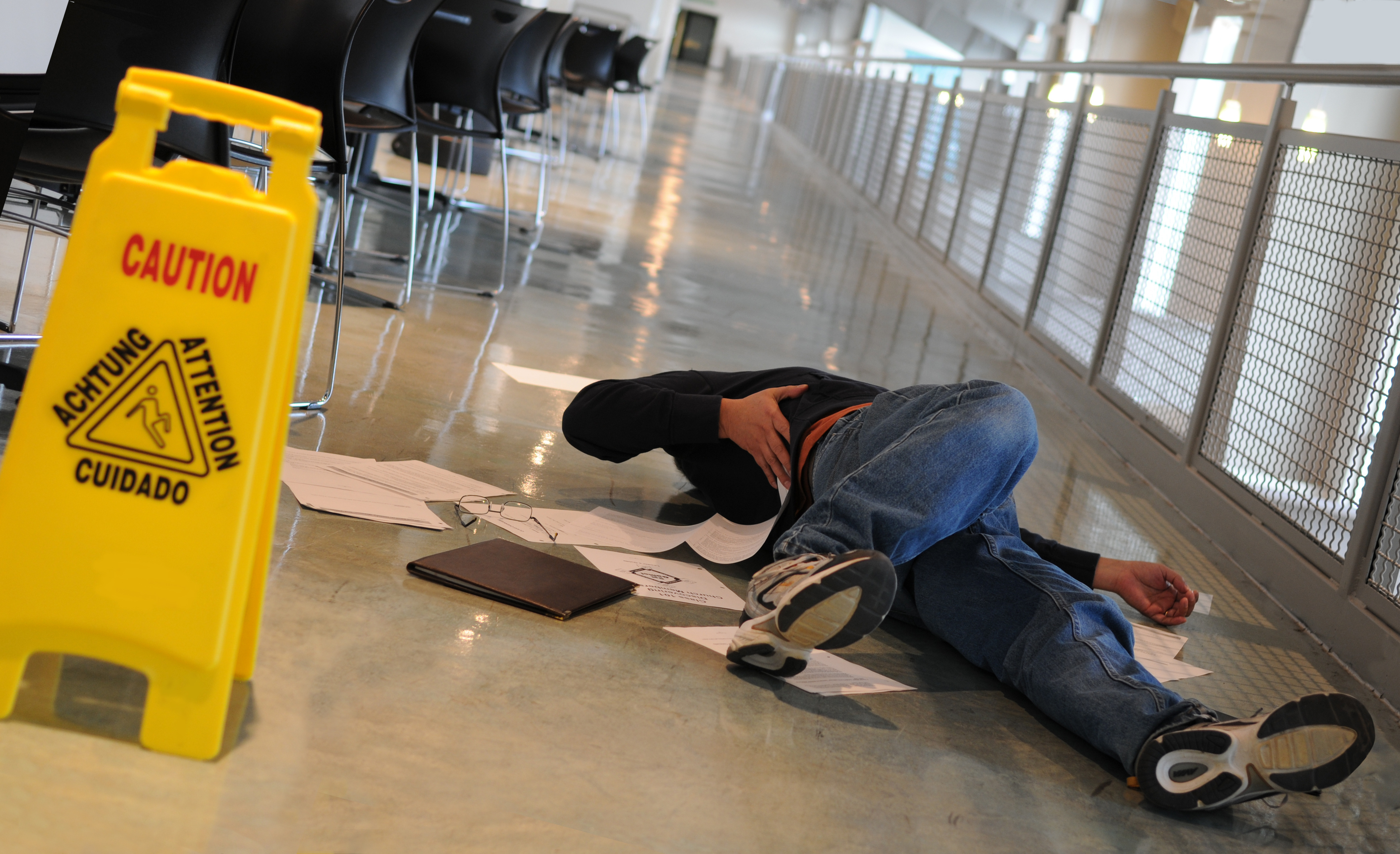 Person injured in a slip and fall accident near a caution wet floor sign.