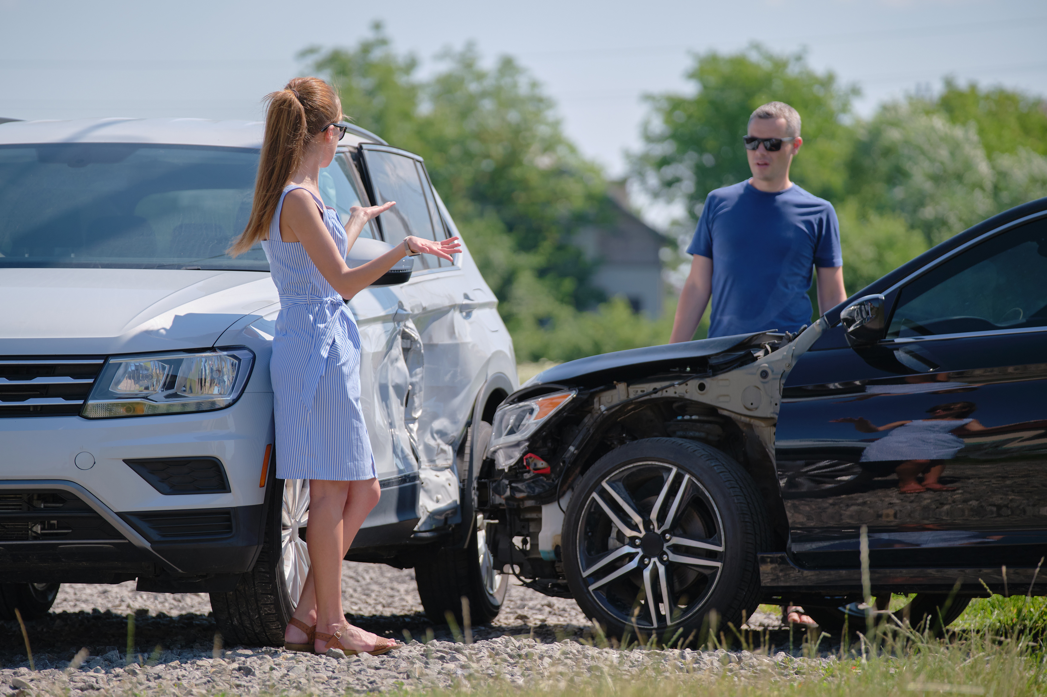 Two drivers standing at the roadside beside a white SUV and a black car with front-end damage after a crash