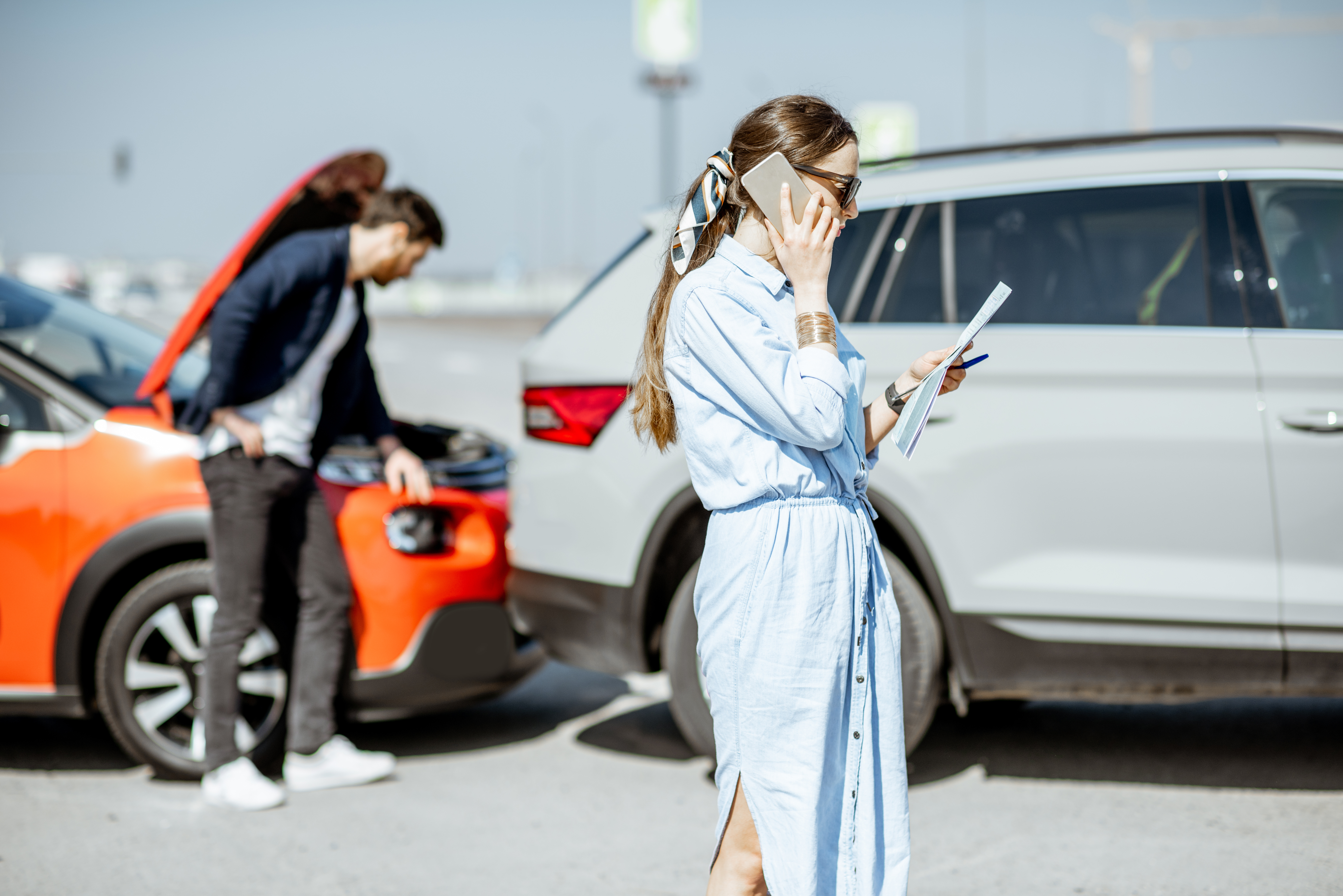Two drivers on their phones exchanging information after a collision between an orange car and a white SUV